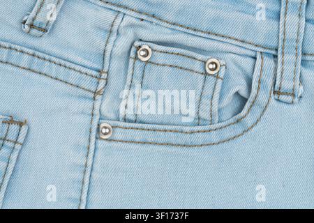 Light blue denim jeans coin pocket with metal rivets. Macro texture of casual clothing fabric. Close up detail of rugged pants material. Cotton textil Stock Photo