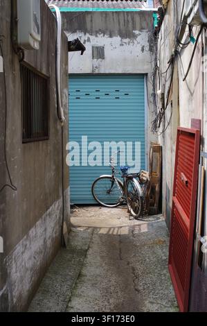 An old bicycle rests against a teal roller shutter door in a narrow Mullae Artist Village alley, South Korea. Stock Photo