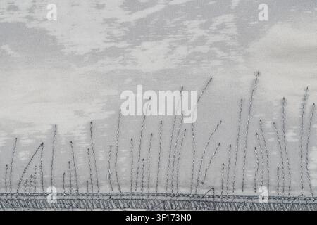 Closeup of hand stitched grass design on light gray fabric. Soft diffused lighting highlights thread texture subtle cloudlike background. Minimalist s Stock Photo
