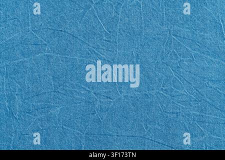 Closeup detail of wrinkled blue denim fabric. Crumpled cotton textile shows visible weave and creases. Faded, casual and worn texture is ideal for des Stock Photo
