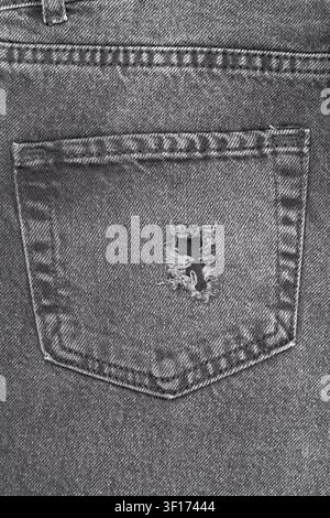 Close up detail of ripped back pocket on worn black denim jeans. Textured fabric with hole and frayed threads. Monochromatic background ideal for fash Stock Photo