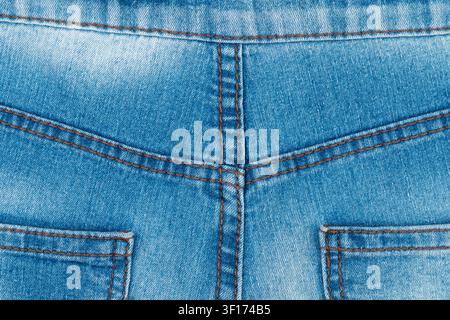 Close up detail of blue jeans fabric. Faded denim texture with symmetrical orange stitching on back yoke and pockets. Casual fashion background for cl Stock Photo