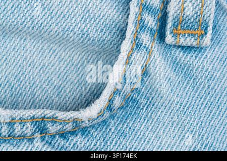 Textured light blue denim closeup featuring yellow stitching frayed jeans front pocket. Woven pattern fabric detail Stock Photo
