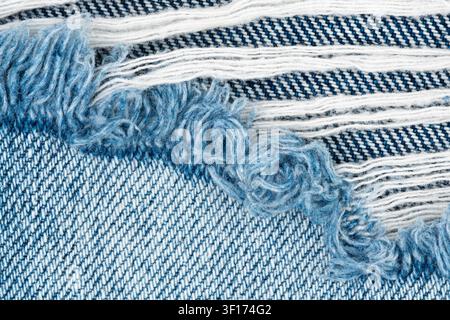 Closeup view of blue denim fabric with distressed ripped texture. Frayed cotton threads and torn material of jeans pants. Detailed background for fash Stock Photo