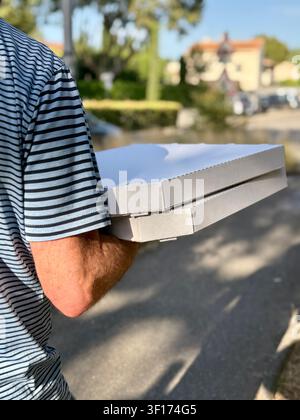 Rear view of a man walking along a street carrying two pizza boxes Stock Photo