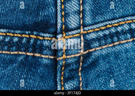 Textured blue denim closeup with contrasting yellow stitching forming geometric patterns. Emphasizes fabric weave, thread detail, rugged style. Ideal Stock Photo