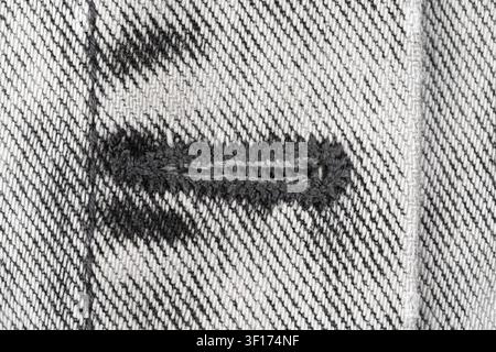 Top view of distressed denim fabric with buttonhole revealing inner texture. Monochrome tones highlight weave pattern of heavyweight denim Stock Photo