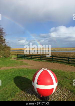 Rainbow over an Old Sea Mine now painted as a charity box for collecting money near the beach, Sonderho, Fanoe, Jutland, Denmark Stock Photo