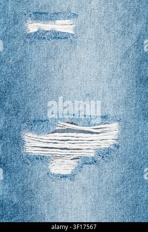 Closeup macro shot of light blue ripped denim fabric. Texture shows worn and torn holes with frayed white threads. Trendy, casual, vintage style backg Stock Photo
