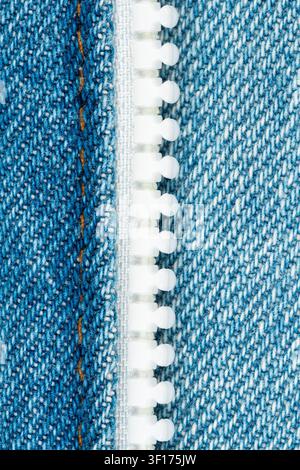 Macro shot of white plastic zipper teeth on blue denim fabric with visible orange stitching. Textured weave clean lighting highlight material detail Stock Photo