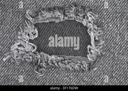 Grey denim fabric with large hole. Distressed jeans texture with frayed threads and worn edges. Rugged casual fashion background for creative design a Stock Photo