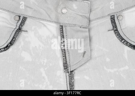 Textured denim fabric with faded wash contrast stitching. Focus on front pocket, button, seam details. Monochrome tones, soft lighting, minimal compos Stock Photo