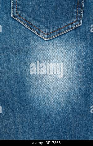 Detailed close up of blue denim fabric. Features classic back pocket with orange stitching. Worn, faded texture with soft central light. Ideal backgro Stock Photo
