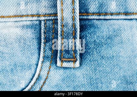 Detailed macro view of light blue denim fabric showing texture, weave, contrasting orange stitching. Focus on belt loop seam construction. Ideal for f Stock Photo