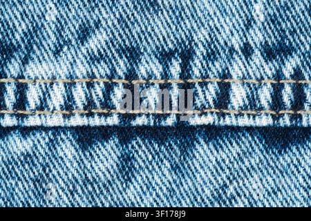Extreme closeup of blue stonewashed denim fabric. Detailed macro shot shows diagonal twill weave, texture and horizontal double seam with yellow stitc Stock Photo