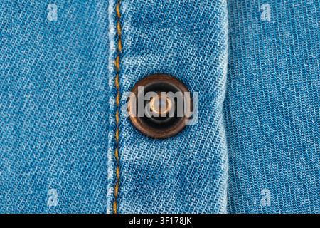 Closeup of metal button on blue denim fabric. Macro shot of jeans texture with visible stitching. Detail of garment construction for fashion design, t Stock Photo