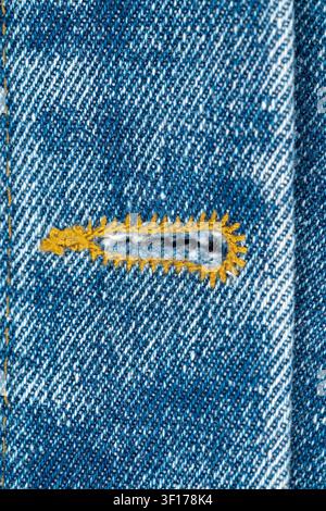 Extreme closeup of buttonhole on blue jeans jacket. Denim fabric shows detailed diagonal weave and texture. Buttonhole is reinforced with thick yellow Stock Photo