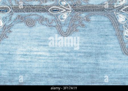 Closeup of light blue denim with ornate gray white embroidery along top edge. Textured weave subtle fading create casual, vintage feel Stock Photo