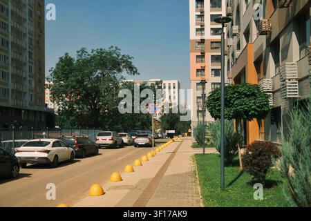 Modern residential street with protective traffic bollards, parked cars, wide pedestrian sidewalk and contemporary apartment buildings in an urban Stock Photo