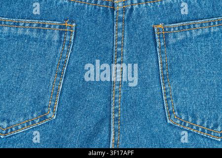 Closeup symmetrical view of back pockets on classic blue jeans. Durable denim fabric shows texture and bright orange stitching provides contrast. Idea Stock Photo