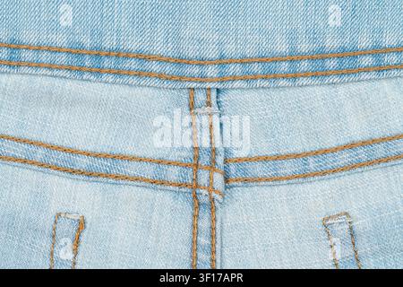 Light blue denim fabric with visible brown thread stitching. Focus on texture, weave, seam details. Casual, durable material. Ideal for fashion, texti Stock Photo