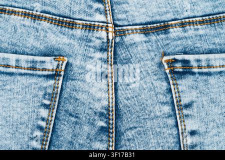 Closeup of light blue acid wash denim texture. Macro shot shows back pockets, center seam and orange stitching. Classic retro 80s style fabric backgro Stock Photo