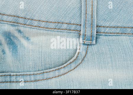 Close up macro shot of light blue denim fabric. Image shows material texture, front jeans pocket detail with double stitching in brown thread and belt Stock Photo