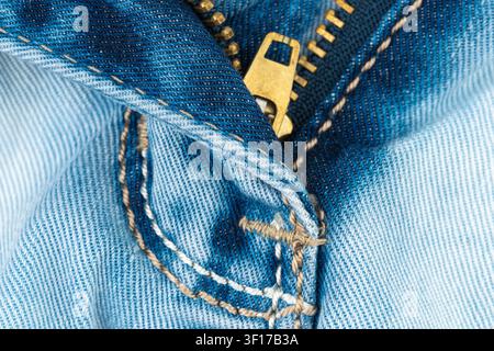 Macro photograph of blue jeans showing detailed denim fabric texture, stitching, metal zipper. Closeup view highlights casual clothing material crafts Stock Photo