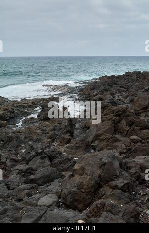 A dramatic coastal landscape showcasing textured basalt rocks and ocean foam, providing an ideal background for nature, environmental, and travel-them Stock Photo