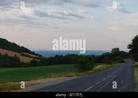 Winding empty rural road through rolling hills overlooking the valley on a cloudy morning in Monts d'Or, France. Stock Photo