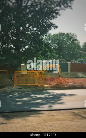 Excavator working at an urban construction site behind orange safety fencing during excavation and underground infrastructure installation in a modern Stock Photo
