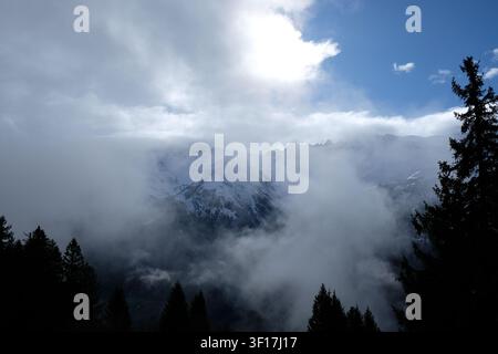 Majestic snow covered alpine peak breaks through swirling mist under a blue sky, ideal for travel, adventure, and nature concepts. Stock Photo