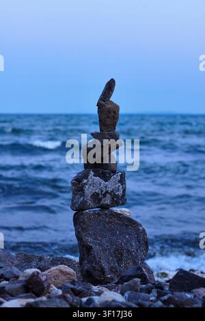 Balanced stones stacked on a seashore with gentle waves and a clear sky during sunset, highlighting natural textures and coastal scenery Stock Photo