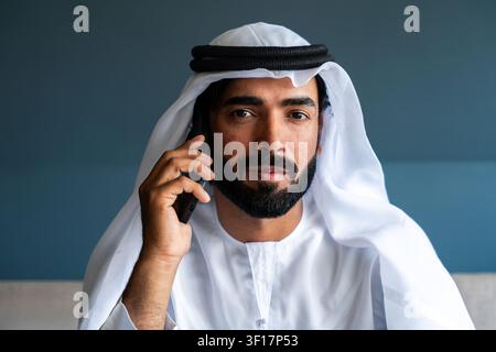 Middle eastern man interacting on a cellphone, wearing a ghutra and agal, portraying modern communication, professional connection, and traditional id Stock Photo