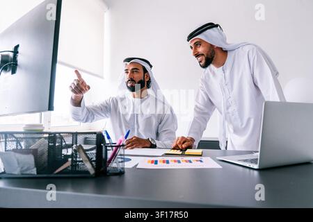 Two arab male professionals wearing traditional clothing collaborating on a business project Stock Photo