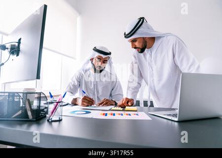 Two arab male professionals collaborating on financial data and business reports, discussing strategies and planning while working in a modern office Stock Photo