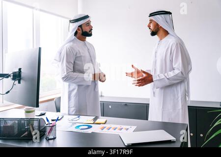 Two arabian business men wearing traditional kandura and ghutra are having a serious discussion about business strategy and financial data, standing i Stock Photo