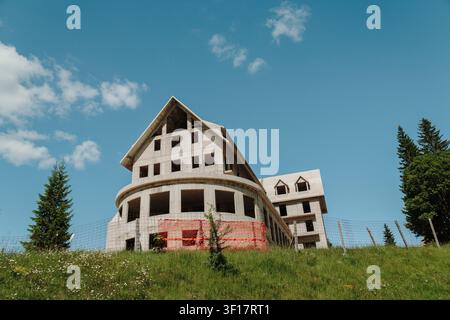 Unfinished concrete hotel building under construction in Zabljak, Montenegro. Large mountain development beneath a clear blue sky. Stock Photo