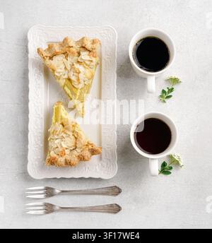 Top view of two delicious slices of homemade rhubarb tart with almond flakes served on a white rectangular plate with two cups of black coffee and vin Stock Photo