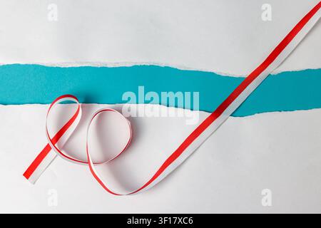 Elegant red and white curled ribbon laid across a white surface with a torn paper edge revealing a vibrant turquoise or teal blue background. High Quality Photo Stock Photo