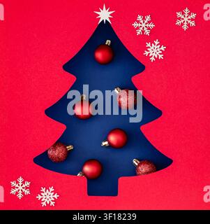 Creative Xmas tree silhouette with red ornaments and snowflakes on blue background. Christmas and New Year concept. Festive holiday backdrop image. Stock Photo