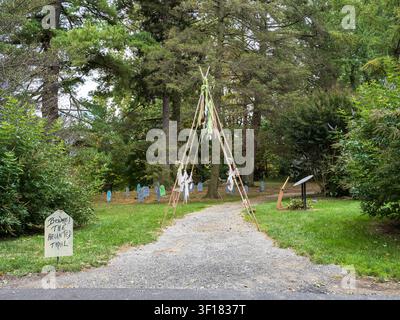 A gravel path leading through a wooded area to a field with colorful grave markers and a 'Beware The Haunted Trail' sign. Stock Photo