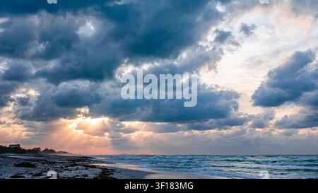 Beautiful sunset over the beach with dramatic clouds and shimmering ocean waves. Stock Photo