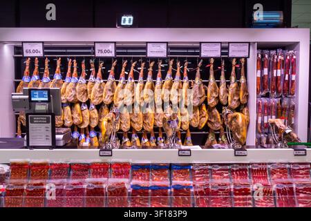 traditional dry-cured Spanish ham legs, commonly known as jamón (such as jamón ibérico or jamón serrano), hanging behind a deli or market counter Stock Photo