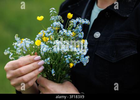 A close-up of a small, delicate bouquet of blue forget-me-nots in a girl's hands. Yellow flowers are among the forget-me-nots. Stock Photo