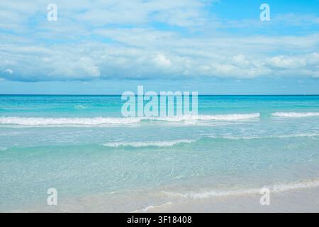 Calm ocean waves gently lap on the sandy shore under a bright blue sky. Stock Photo
