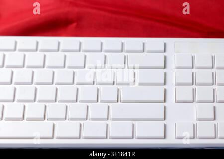 A horizontal wide shot captures a clean, pristine white computer keyboard with empty keys, set against a blurred vibrant red fabric background. This shot highlights the contrast between the white technological device and the soft red texture, conveying concepts of e-commerce, remote work, programming, and copy space. High Quality Photo Stock Photo