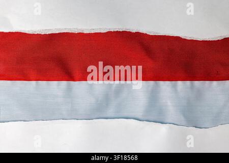 A detailed close-up abstract view showing a torn edge of white paper uncovering a bold red and white striped fabric material underneath. The prominent texture of the woven textile and the fibrous torn paper edge create an engaging backdrop ideal for national concepts or design backgrounds. High Quality Photo Stock Photo