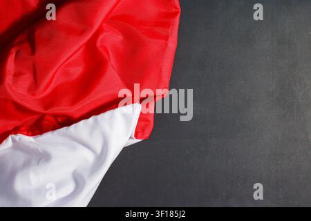 A high-angle flat lay shot displays a crinkled red and white textile material positioned on the left side, leaving ample negative space on a dark grey wooden surface. This composition is ideal for presentations, patriotic themes, text placement, and clean graphic design layouts. High Quality Photo Stock Photo