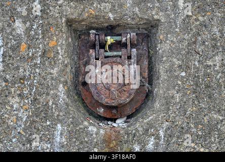 Rusty hinged cover over a drainage pipe in a concrete sea wall Stock Photo